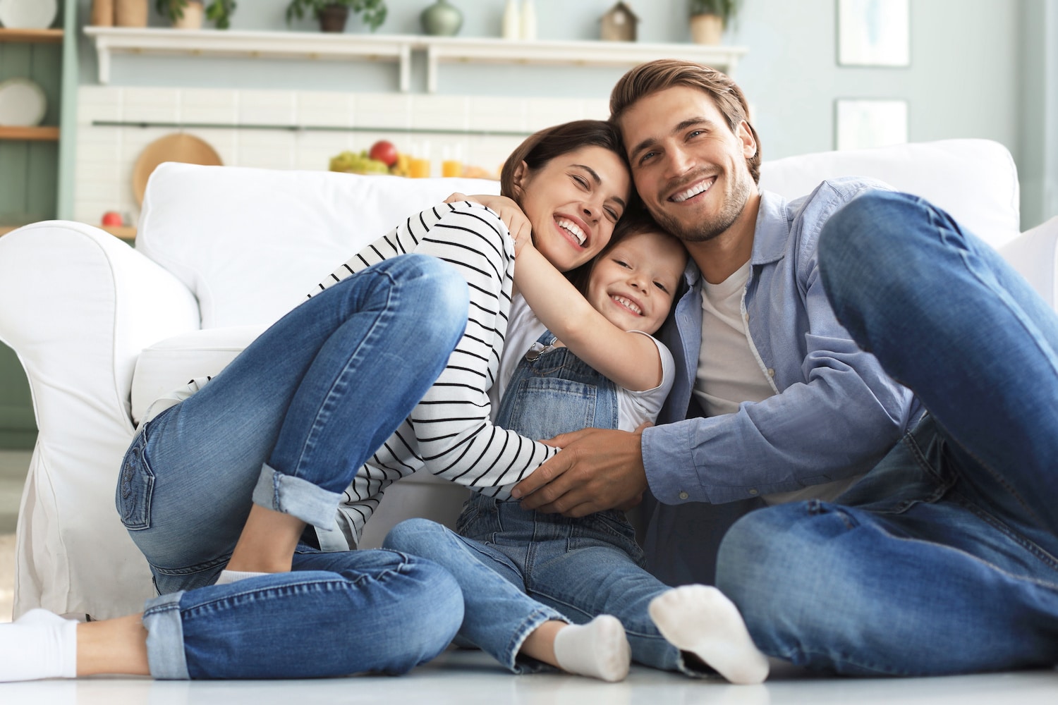 Young family with small daughter pose relax on floor in living room, smiling little girl kid hug embrace parents, show love and gratitude, rest at home together